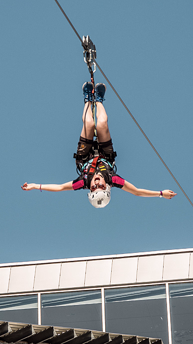 Person som henger opp ned på en zipline med utstrakte armer mot en blå himmel
