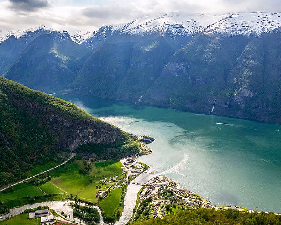 Landsby ved en fjord omgitt av grønne åser og høye snødekte fjell
