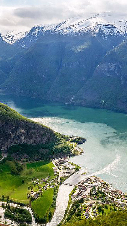 Landsby ved en fjord omgitt av grønne åser og høye snødekte fjell