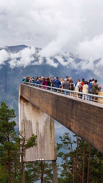 Mennesker på en utsiktsplattform i tre med utsikt over grønn skog og fjell
