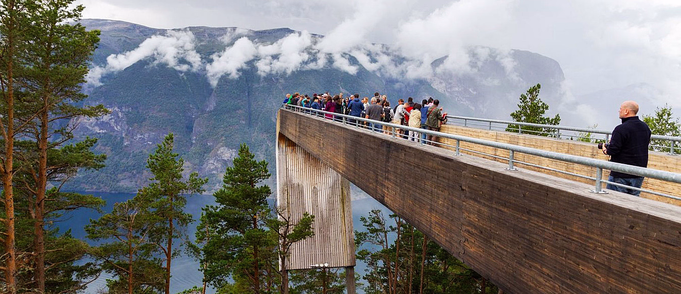 Mennesker på en utsiktsplattform i tre med utsikt over grønn skog og fjell