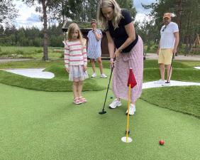 En kvinne spiller minigolf mens en mann og to barn ser på utendørs