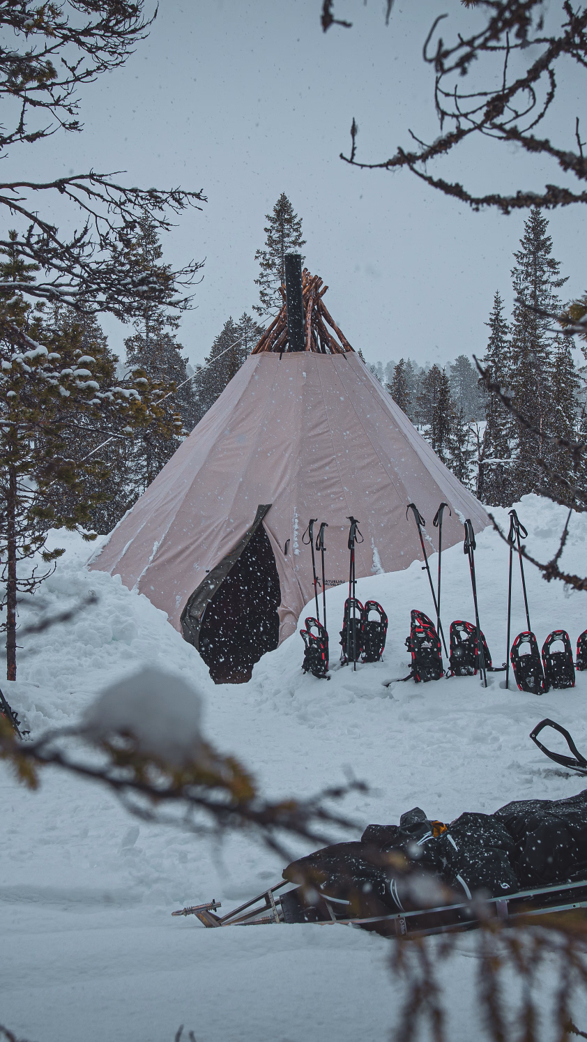 Lavvo i snødekt skog med truger og snøscooter parkert utenfor