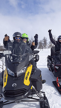 Fire personer på snøscootere i et snødekt landskap med armene i været