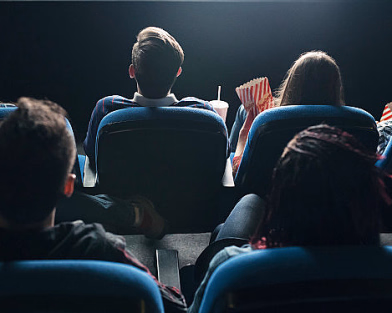 Personer sett bakfra som sitter i en kinosal med popcorn og drikke