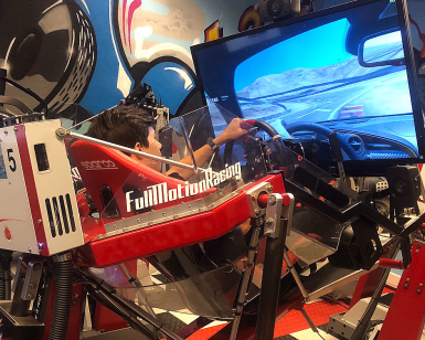 Person i en rød racingsimulator med ratt foran en skjerm som viser et bilspill