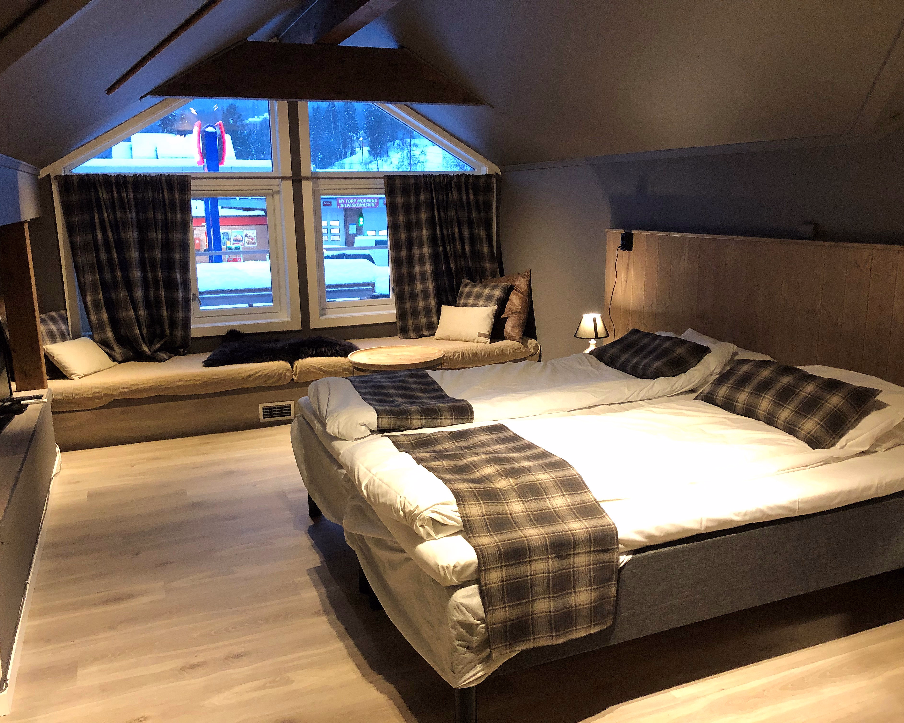 Soverom med skråtak, senger med rutete puter og sittebenk ved et vindu med utsikt til snø