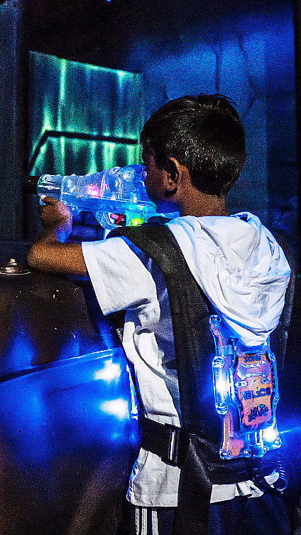Barn med lysende lekepistol og lysende vest ved en rusten bil i neonlys