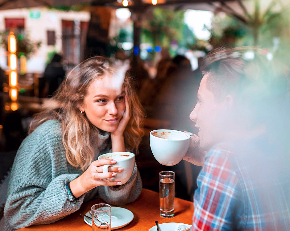 Kvinne og mann sitter ved et kafébord og holder hvite kaffekopper