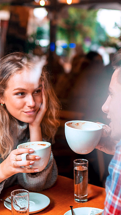 Kvinne og mann sitter ved et kafébord og holder hvite kaffekopper