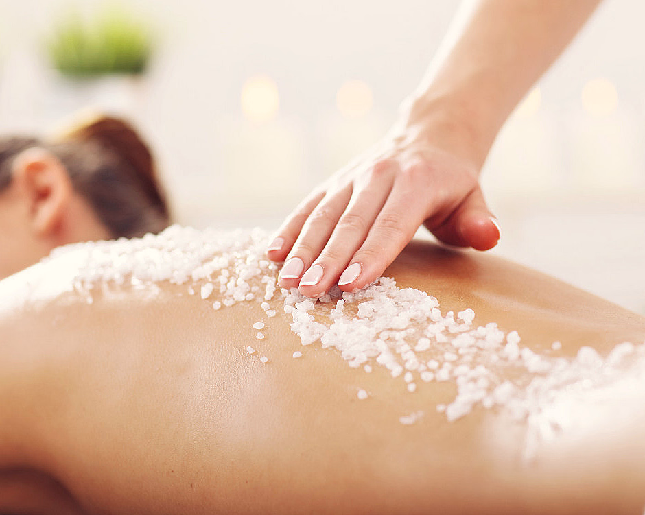 En hånd masserer grovt salt på en rygg i et spa med planter og tente lys