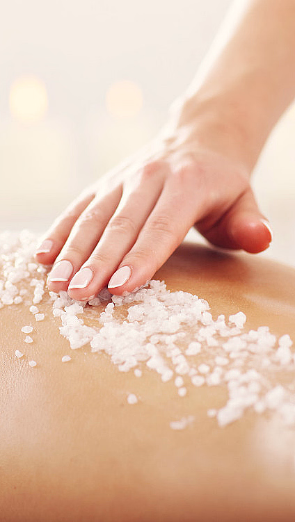 En hånd masserer grovt salt på en rygg i et spa med planter og tente lys