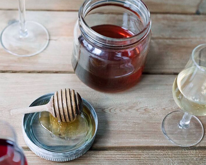 Glass med mørk væske, honningdipper og smaksglass på et trebord