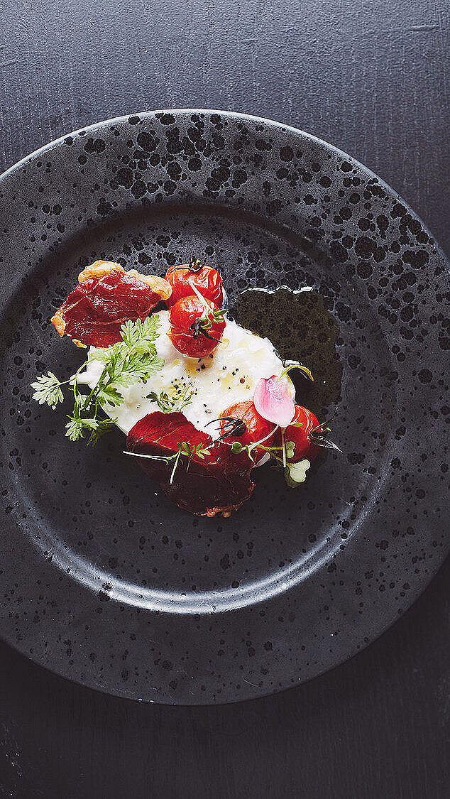 Anrettet tallerken med burrata, cherrytomater, urter og tørket kjøtt på en mørk overflate