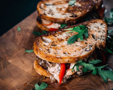 To ristede sandwicher med fyll og ruccola på et skjærebrett av tre