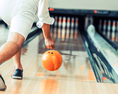 En person kaster en oransje bowlingkule nedover en bowlingbane mot kjeglene