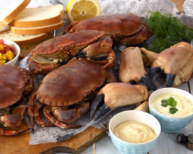 Kokte krabber servert på et trefjøl med loff, sitron, sauser og en hammer