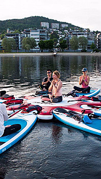 Gruppe mennesker som praktiserer yoga på SUP-brett i en sirkel på vannet
