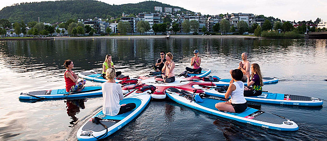 Gruppe mennesker som praktiserer yoga på SUP-brett i en sirkel på vannet