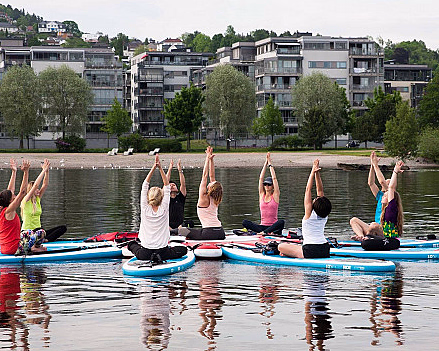 En gruppe mennesker gjør yoga på paddleboards i en sirkel på vannet