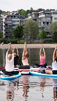 En gruppe mennesker gjør yoga på paddleboards i en sirkel på vannet