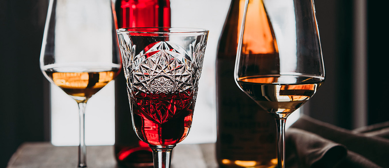 Tre glass med rød og hvit vin foran to flasker på et bord