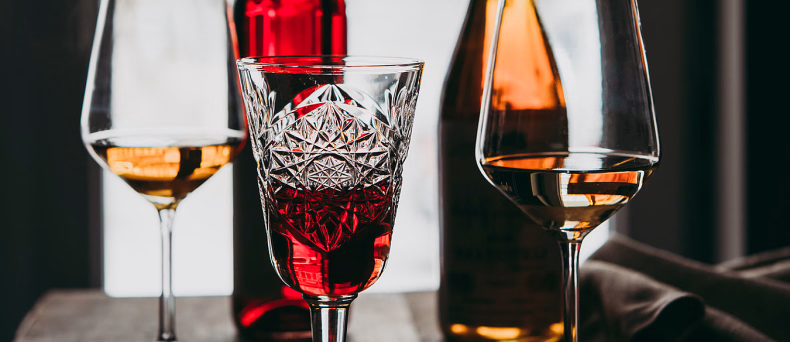 Tre glass med rød og hvit vin foran to flasker på et bord