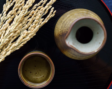 Sake-karaffel, en liten kopp og tørkede risaks på et sort brett sett ovenfra