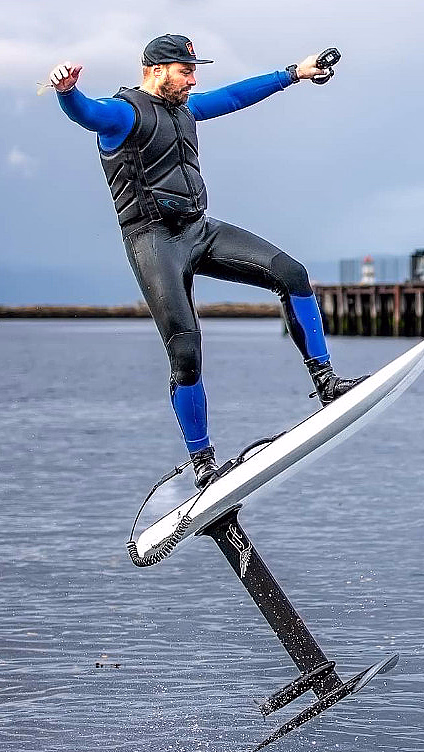 Person i våtdrakt på et hydrofoil-surfebrett over vannet med en brygge i bakgrunnen