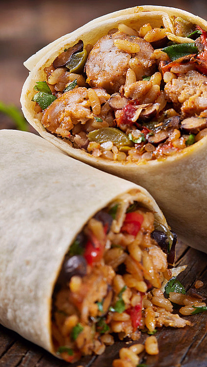 Halvert burrito på trefjøl fylt med ris, bønner, kjøtt og grønnsaker, med lime og rød saus