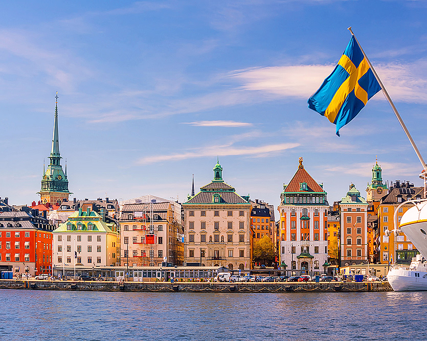 Fargerike bygninger ved vannet med et kirketårn og et svensk flagg på en båt