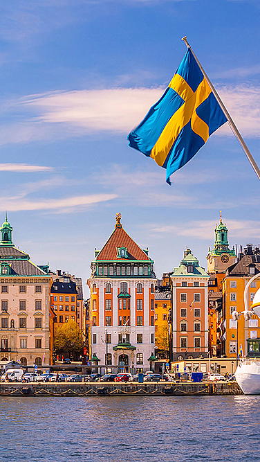 Fargerike bygninger ved vannet med et kirketårn og et svensk flagg på en båt
