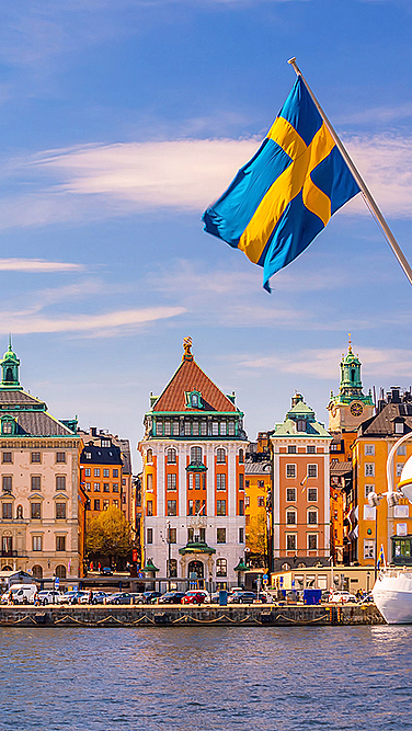 Fargerike bygninger ved vannet med et kirketårn og et svensk flagg på en båt