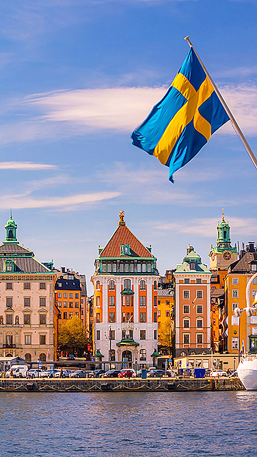 Fargerike bygninger ved vannet med et svensk flagg i forgrunnen