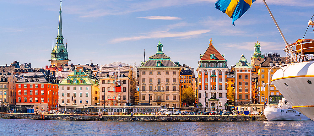 Fargerike bygninger ved vannet med et svensk flagg i forgrunnen