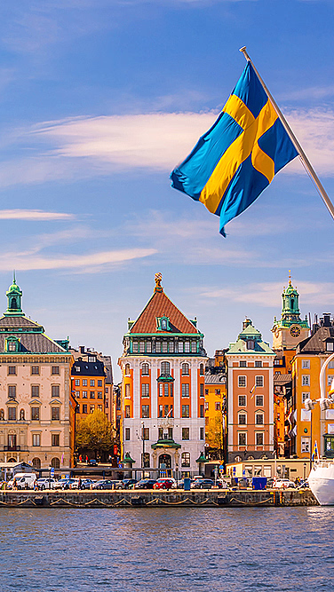 Fargerike bygninger ved vannet med et svensk flagg i forgrunnen