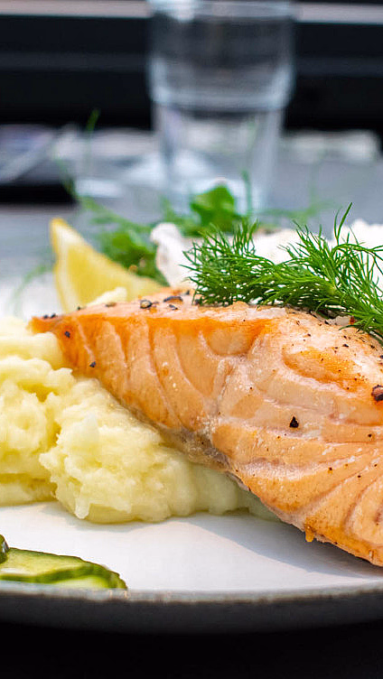 Grillet laks med potetmos, agurk, sitron og saus på en hvit tallerken