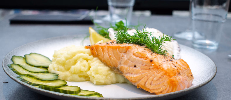 Grillet laks med potetmos, agurk, sitron og saus på en hvit tallerken