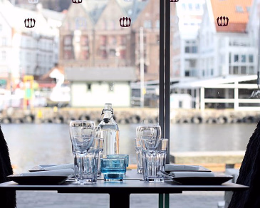 Dekket bord med glass og tallerkener ved et vindu med utsikt over en havn