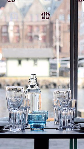Dekket bord med glass og tallerkener ved et vindu med utsikt over en havn