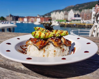 Sushi med avokado og sesamfrø på et trebord med sjø og fargerike hus i bakgrunnen