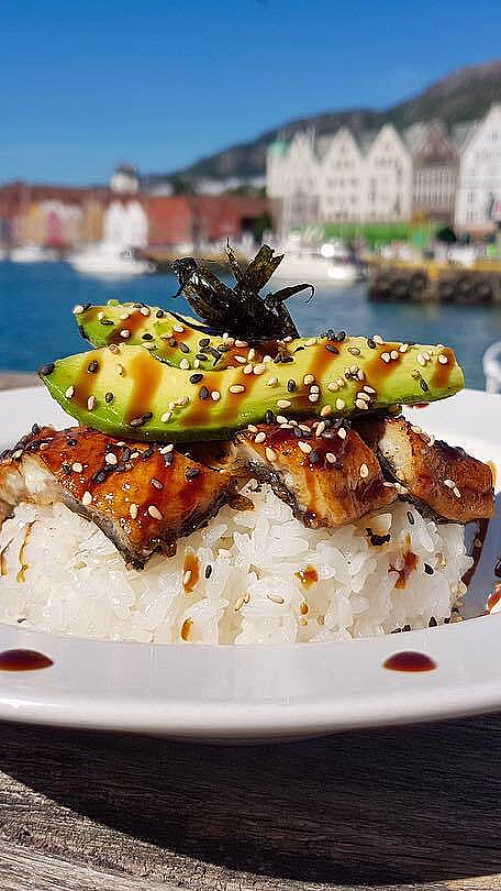 Sushi med avokado og sesamfrø på et trebord med sjø og fargerike hus i bakgrunnen