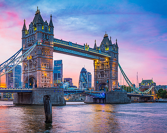 Opplyst Tower Bridge over elven ved solnedgang med moderne bygninger i bakgrunnen