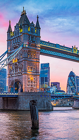 Opplyst Tower Bridge over elven ved solnedgang med moderne bygninger i bakgrunnen