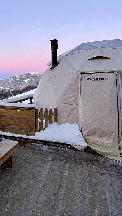 Hvit Arctic Dome på treterrasse i snødekt fjellandskap under rosa og blå kveldshimmel