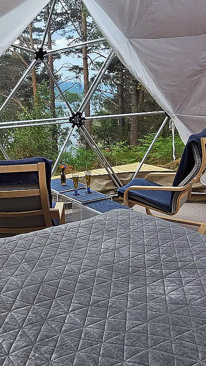 Seng og stoler i en kuppelhytte med utsikt mot trær gjennom et vindu