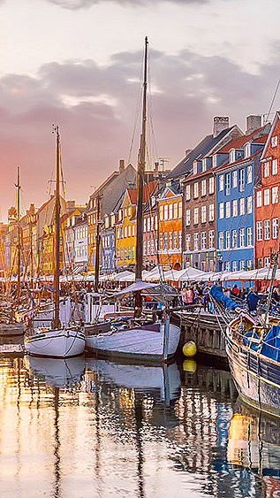 Fargerike bygninger langs en kanal med båter under en rosa og oransje solnedgang