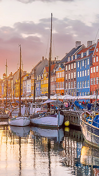 Fargerike bygninger langs en kanal med båter under en rosa og oransje solnedgang