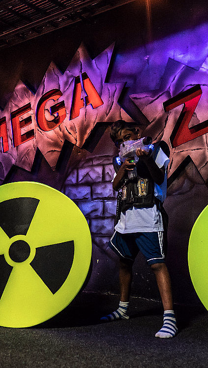 Person med laserpistol og vest foran en vegg med teksten MEGA ZONE og varselskilt