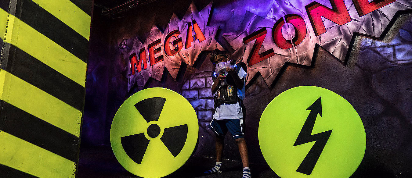 Person med laserpistol og vest foran en vegg med teksten MEGA ZONE og varselskilt